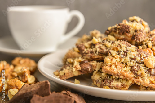 Homemade chocolate toffee nut cookies on a white plate with a ingredients and a cup of coffee in the background on a dark rustic wood table.