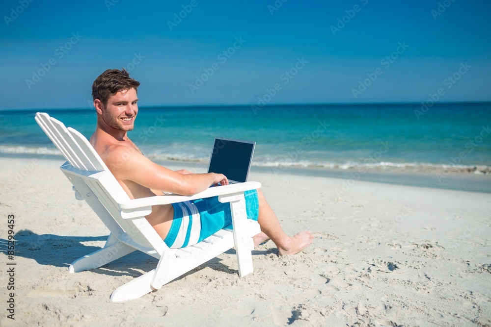 Man using laptop on deck chair at the beach