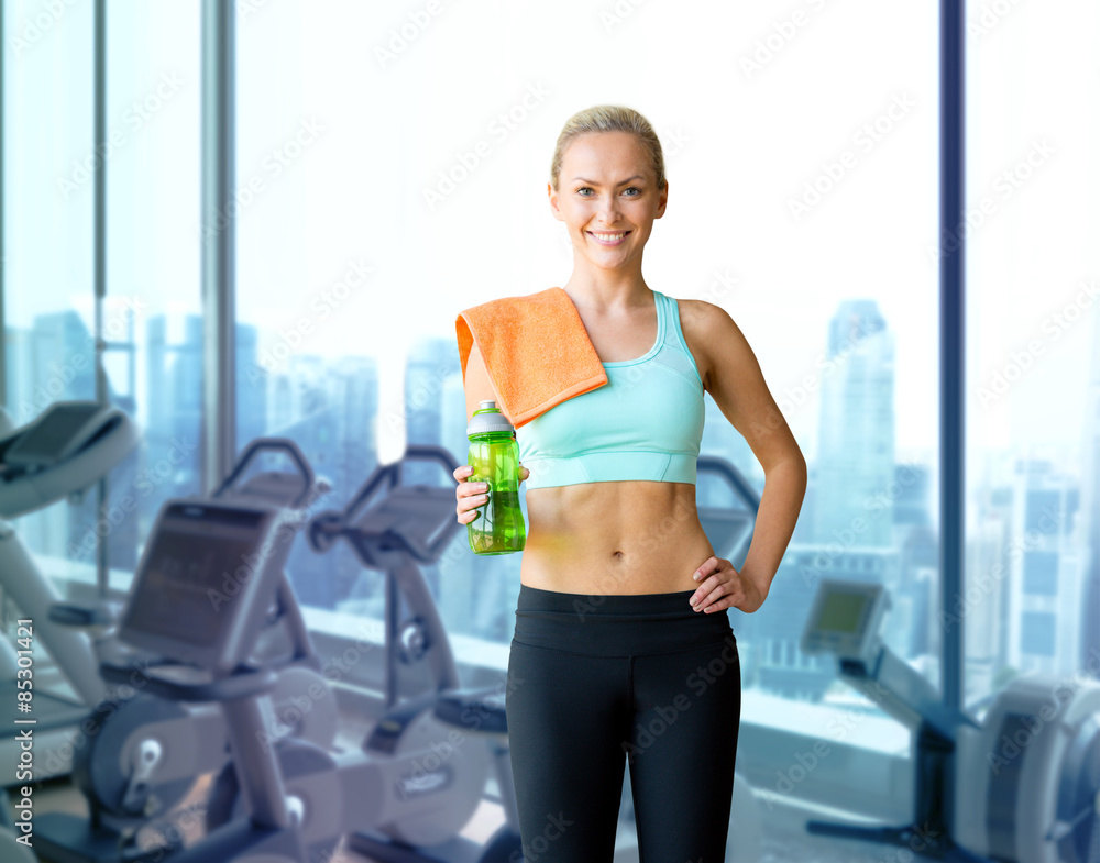 Fototapeta premium happy woman with bottle of water and towel in gym