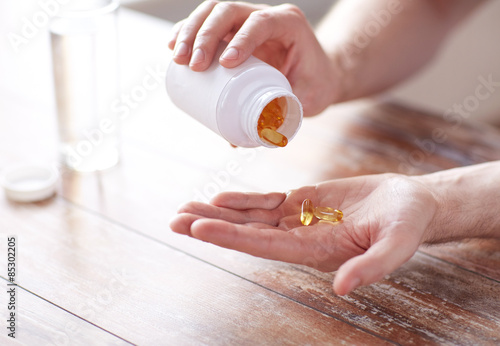 Fotografija close up of man pouring fish oil capsules to hand