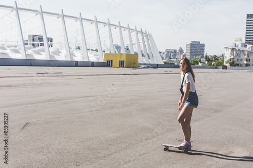 cool young and beautiful caucasian blonde hipster skater girl wearing denim shorts posing smiling and having fun outside while skating with her cute little skateboard summer day