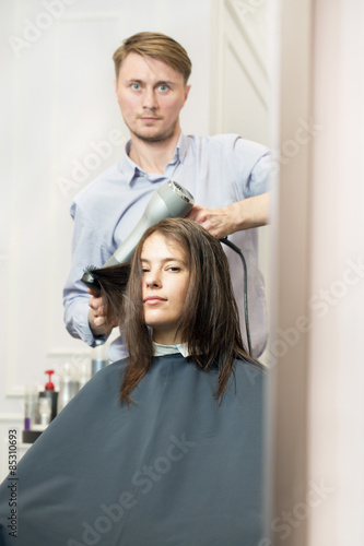 Young woman having her haircut by a handsome hairdresser