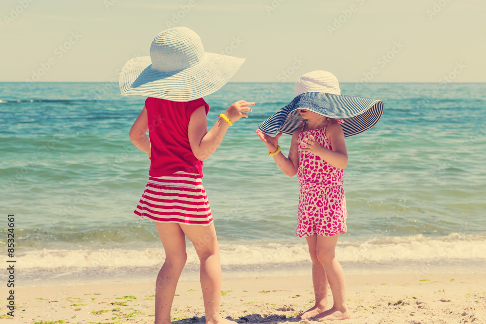 Beautiful funny little girls (sisters) in large hats on the beac
