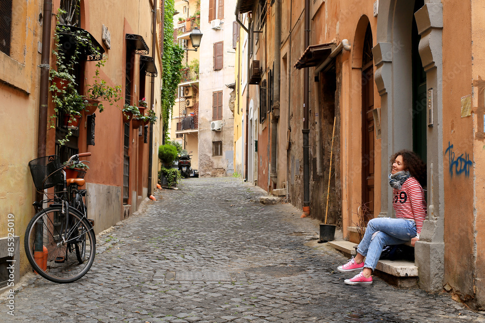 Fototapeta Dziewczyna siedzi w domu na małej włoskiej ulicy