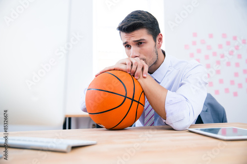 Pensive businessman sitting at the table with ball