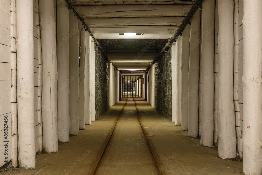 Long mineshaft hallway with wood support beams, railroad tracks, and metal gate. Wieliczka Salt Mine - Krakow, Poland.