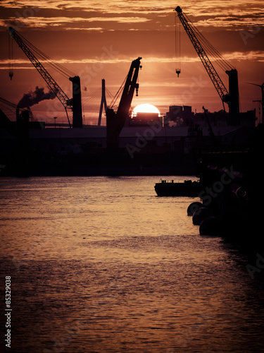 Germany, Hamburg, Silhouettes of harbor cranes at sunset, Koehlbrand bridge in the background photo