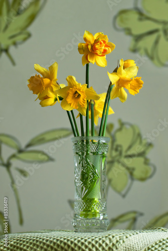 Bouquet yellow daffodils in a crystal vase on a light background.
