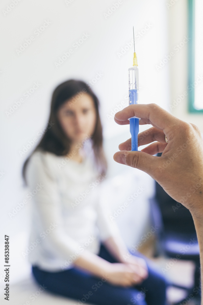 Doctor preparing a syringe with patient in the background Doctor preparing a syringe with patient in the background