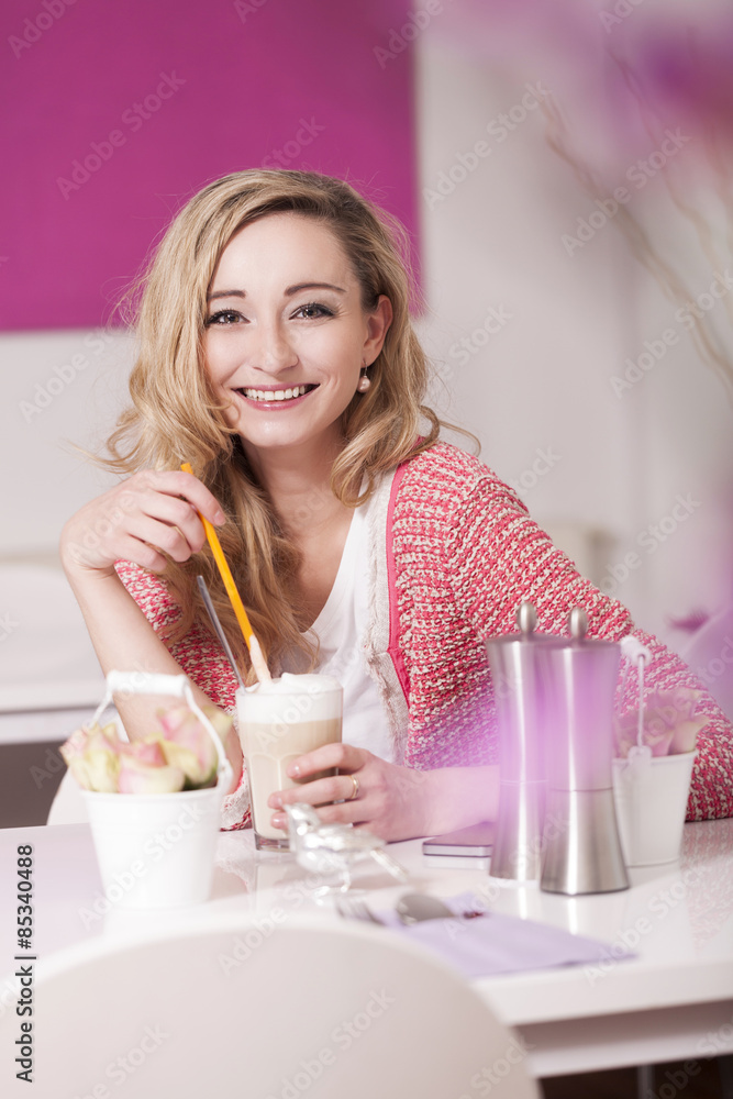 Happy blond woman sitting in a coffee shop with Latte Macchiato
