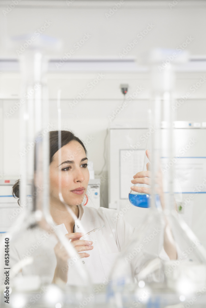 Young scientist in laboratory judging blue liquid in flask Young scientist in laboratory judging blue liquid in flask