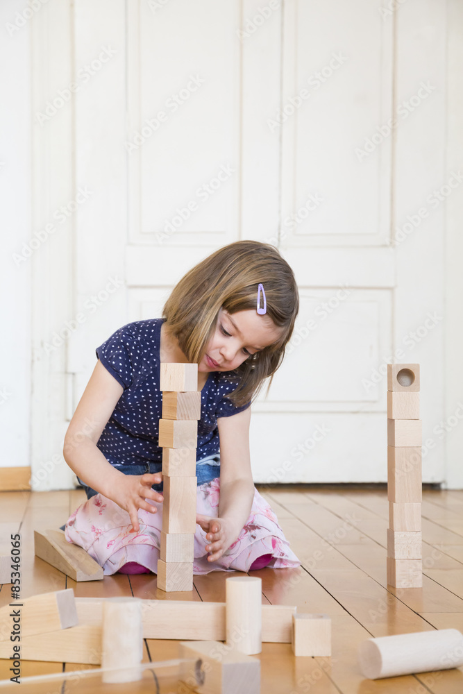 Little girl crouching on floor playing with wooden building bricks Little girl crouching on floor playing with wooden building bricks
