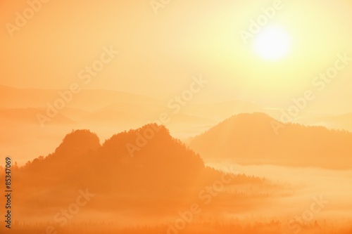 Misty landscape with fog between hills and orange sky within sunrise