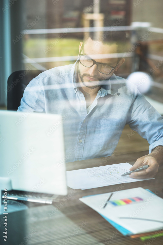 Young man behind windowpane working at computer