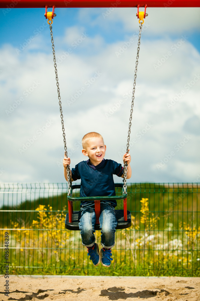 Little blonde boy child having fun on a swing outdoor
