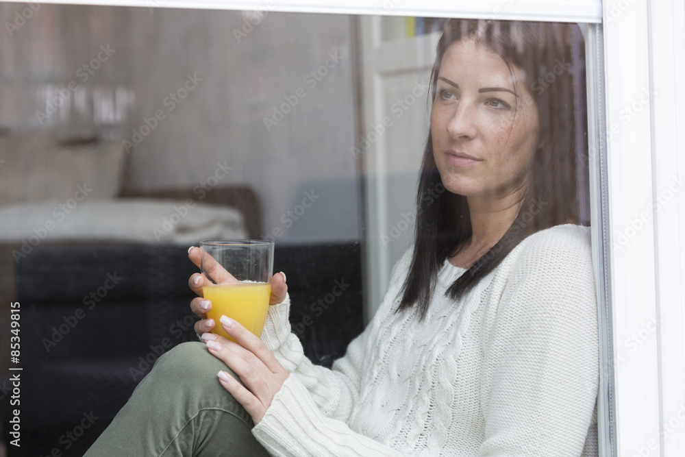 Woman with glass of orange juice looking through window Woman with glass of orange juice looking through window