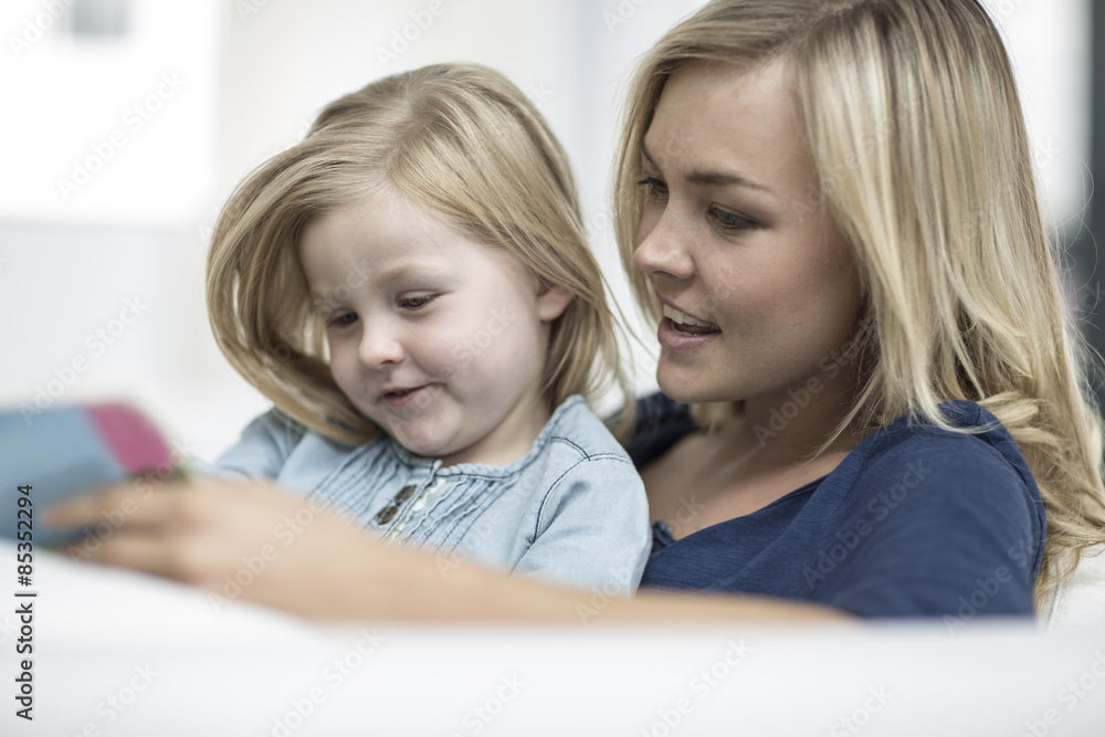 Mother and little daughter sitting on a couch reading a book Mother and little daughter sitting on a couch reading a book