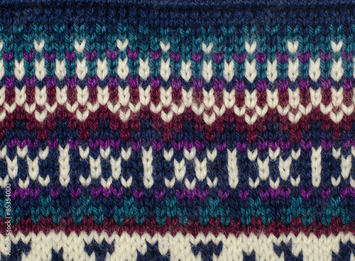 Close up on knit woolen texture. Dark blue, red, purple and white in a line shapes pattern as a background.