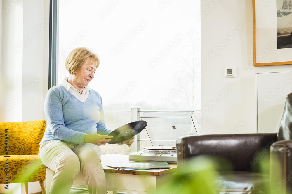 Senior woman at home putting record on record player Senior woman at home putting record on record player