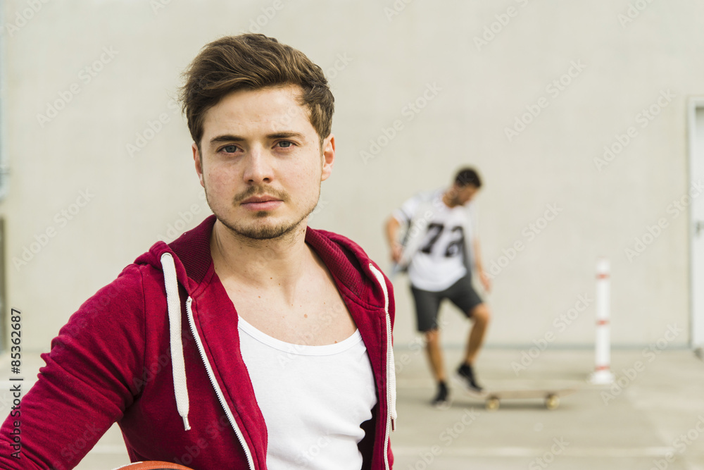 Portrait of young man and man with skateboard in background Portrait of young man and man with skateboard in background