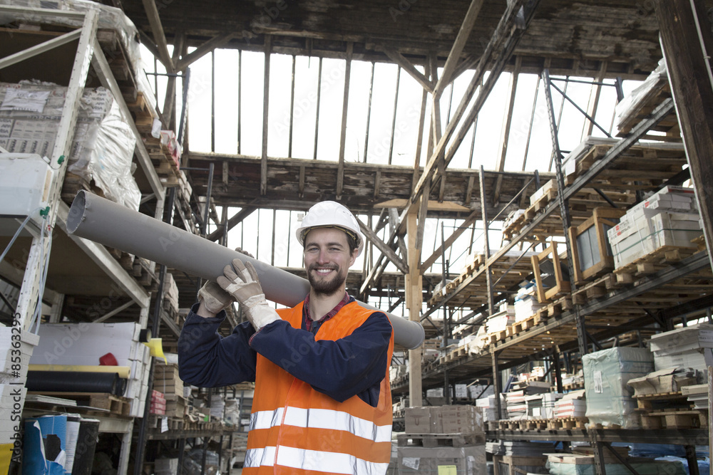 Smiling warehouseman in storehouse carrying pipe Smiling warehouseman in storehouse carrying pipe