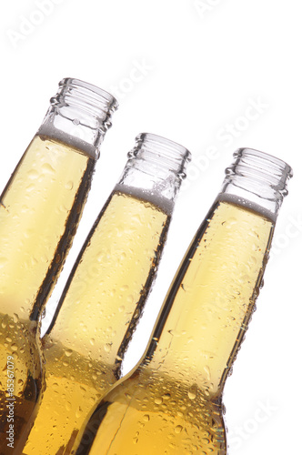 Closeup of three clear beer bottles covered with condensation, over white.