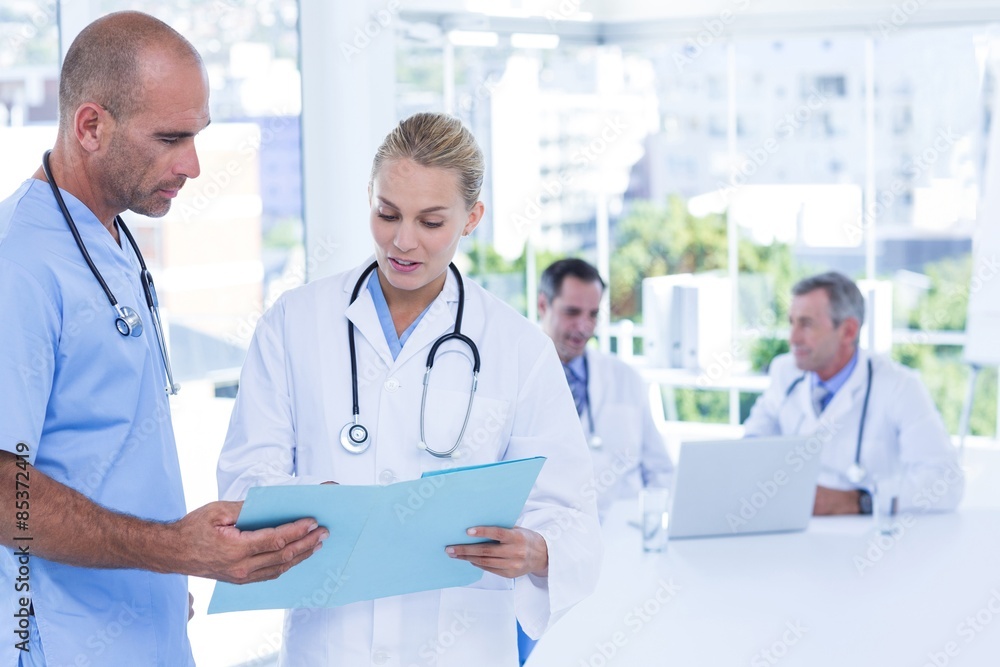 Two doctors holding clipboard while their colleagues working Two doctors holding clipboard while their colleagues working