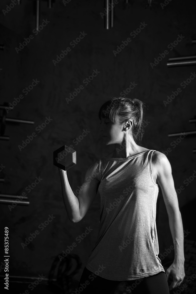 Fitness,Strong young woman poising with dumbbell on black background B&W in studio