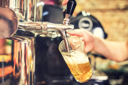 Canvas Print barman hand at beer tap pouring a draught lager beer serving in a restaurant or