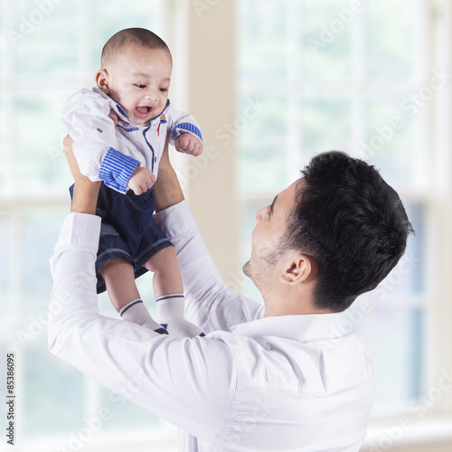 Happy father lift up his baby near the window