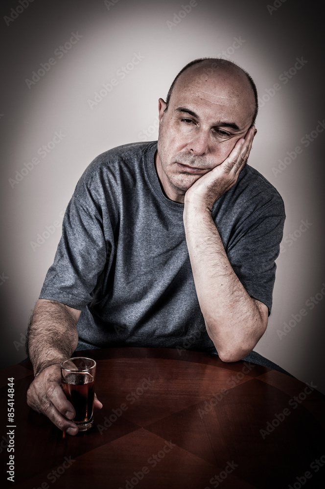 Drunk man sitting at the table, leaning his head on the hand and holding a  glass of alcohol drink Stock Photo | Adobe Stock