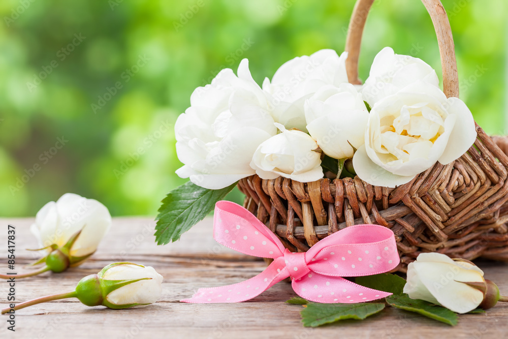 Rustic wicker basket with wild rose flowers and pink ribbon.