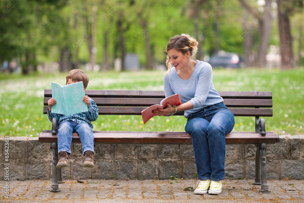 Young woman and cute little boy reading books in a park and talking Young woman and cute little boy reading books in a park and talking