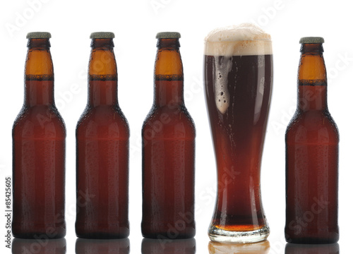 Four Brown Beer Bottles and a Full Glass with foam dripping down the side on a white background.
