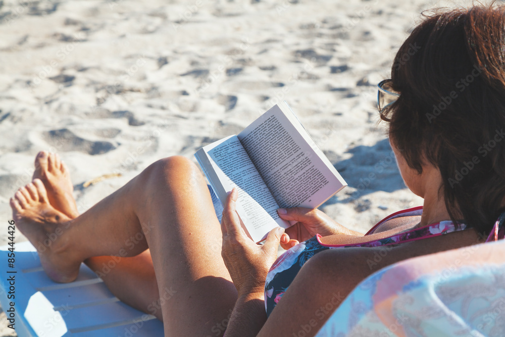 Elderly woman reading book on beach