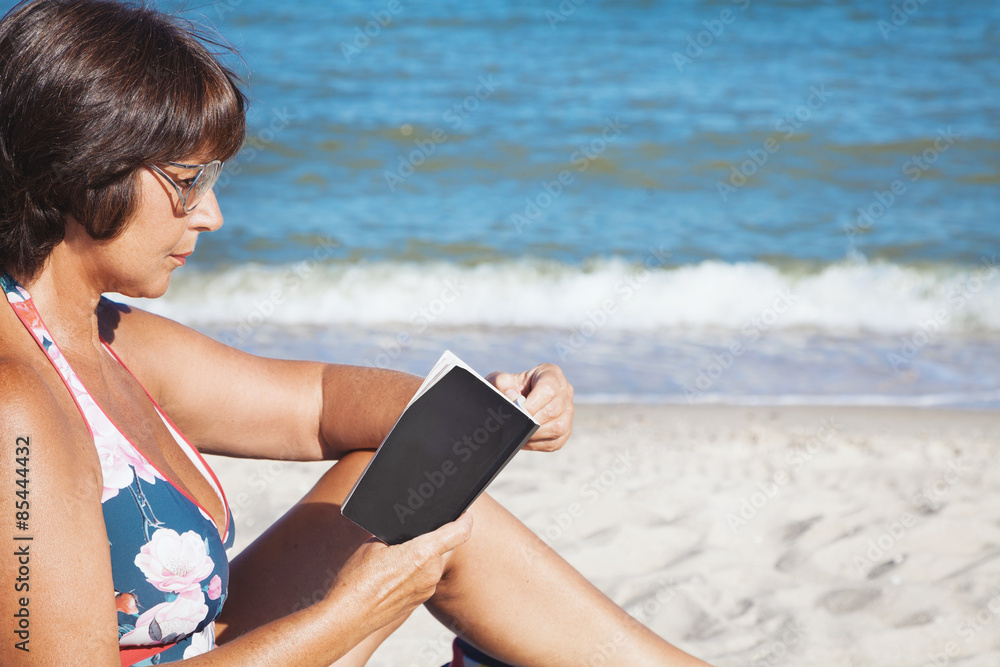 Elderly woman reading book on beach
