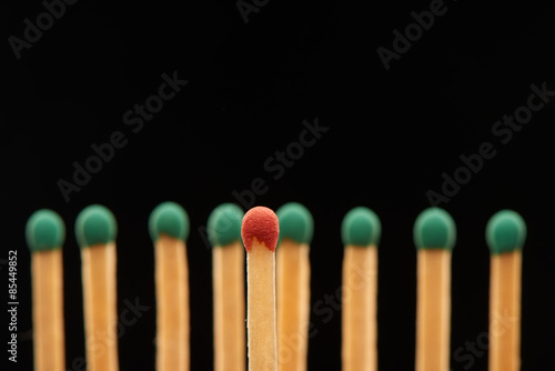 Red wooden match standing in front of eight green matches