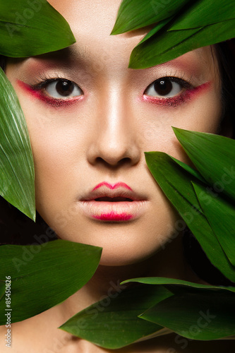 Beautiful Asian girl with a bright make-up art in green leaves