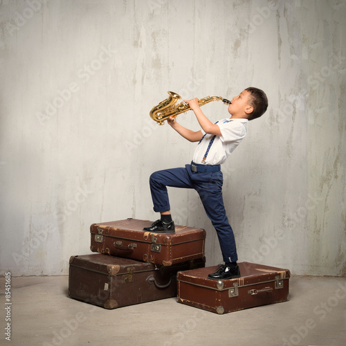 six years old boy stand on retro siuitcases and play sax