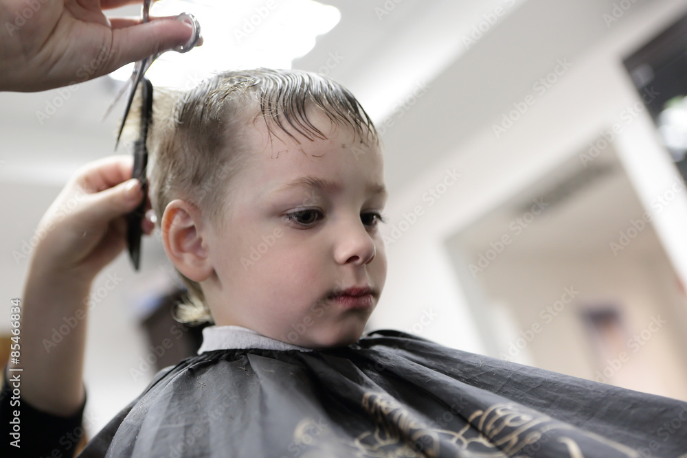 Fototapeta premium Barber cutting hair of a kid