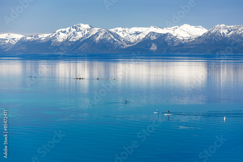 Paddle boarding calm Lake Tahoe with view on Sierra Nevada snowy mountains. 