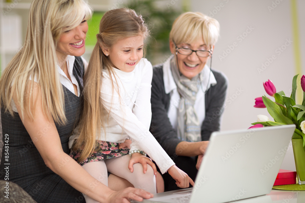 Little girl using laptop with mother and grandmother Little girl using laptop with mother and grandmother