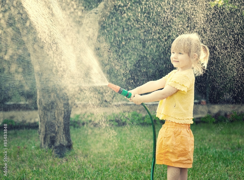 Little girl playing in the garden pouring all the water from a g