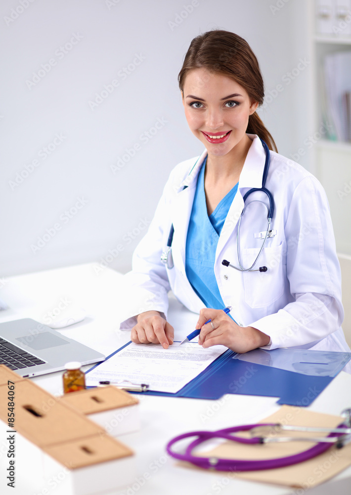 Beautiful young smiling female doctor sitting at the desk and