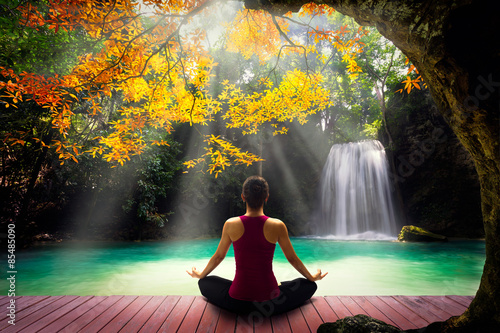 Young woman in yoga pose sitting near waterfall, Rear view