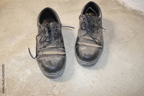 Vieilles chaussures noires poussiéreuses sur sol de béton.