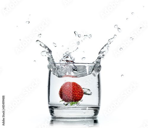 A fresh strawberry splashing water in a glass