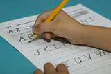 Asian boy's hand starts writing alphabet A with a yellow pencil on a blue table