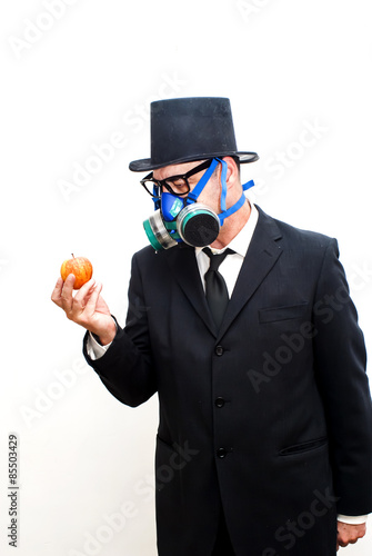 Businessman with gas mask and hat looking at an apple in his hand