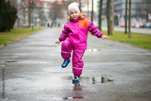 Little happy girl jumping in puddle